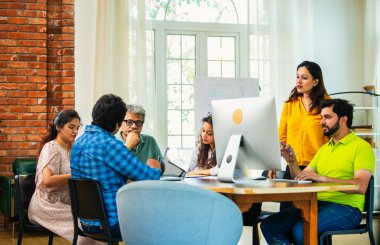 Hintli Asyalı genç iş adamları proje stratejisi üzerinde çalışan, belgeleri analiz eden, dizüstü bilgisayarda çalışan, iş geliştirme başarısı için samimi modern ofiste beyin fırtınası yapan bir ekip kurdular.