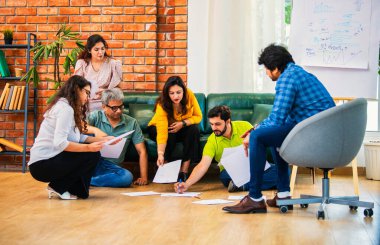 Hindistanlı Asyalı genç iş ortakları yeni ortaklar belgelerle önemli projeler planlarken modern, samimi, katılımcı ve takım çalışması olan ofiste birlikte oturuyorlar.
