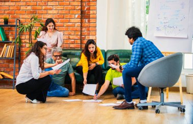 Hindistanlı Asyalı genç iş ortakları yeni ortaklar belgelerle önemli projeler planlarken modern, samimi, katılımcı ve takım çalışması olan ofiste birlikte oturuyorlar.