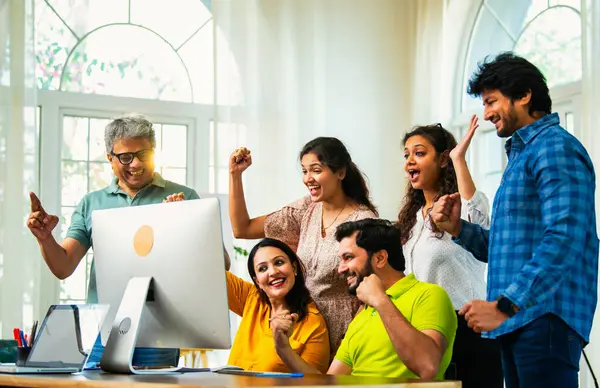 Hintli Asyalı genç iş adamları ya da teknoloji ortakları bilgisayarda çalışıyor, birden başarıyı beşlik çakarak kutluyorlar, modern rahat ofiste dizüstü bilgisayarla masada oturuyorlar.