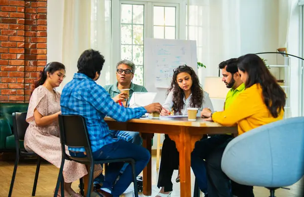 Hintli Asyalı genç iş adamları proje stratejisi üzerinde çalışan, belgeleri analiz eden, dizüstü bilgisayarda çalışan, iş geliştirme başarısı için samimi modern ofiste beyin fırtınası yapan bir ekip kurdular.