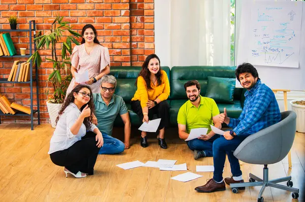 Hindistanlı Asyalı genç iş ortakları yeni ortaklar belgelerle önemli projeler planlarken modern, samimi, katılımcı ve takım çalışması olan ofiste birlikte oturuyorlar.