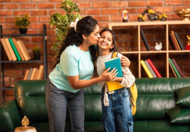 Hintli bir anne, kızının okula gitmesine yardım etmek için kitap paketliyor, okul çantasına beslenme çantası koyuyor, ona sevgiyle sarılıyor ve sıcak bir ev ortamında şefkatle onu uğurluyor.