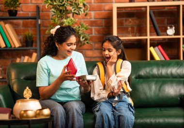 Hintli Asyalı genç anne okuldan önce sevgi dolu bir şekilde küçük kızına beslenme çantasını açar ve birlikte şık, modern bir evde otururken heyecanla gülümsemesini sağlar.