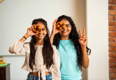 Hintli Asyalı genç bir anne ve şirin küçük bir kız kanepede oturuyor modern bir evde, neşeyle yuvarlak bir çörek tutuyor, delikten bakıyor, gülümsüyor ve iyi bir el hareketi yapıyor.