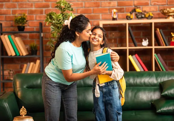 Hintli bir anne, kızının okula gitmesine yardım etmek için kitap paketliyor, okul çantasına beslenme çantası koyuyor, ona sevgiyle sarılıyor ve sıcak bir ev ortamında şefkatle onu uğurluyor.
