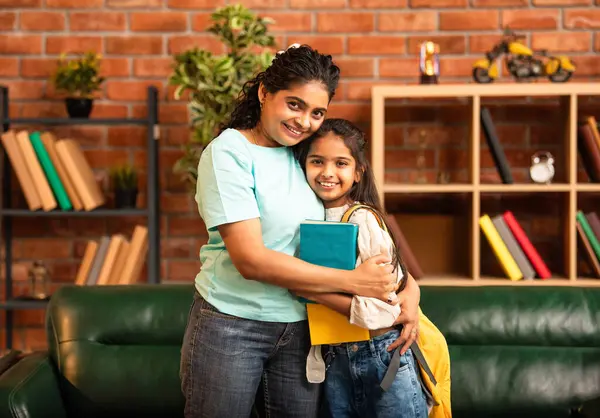 Hintli bir anne, kızının okula gitmesine yardım etmek için kitap paketliyor, okul çantasına beslenme çantası koyuyor, ona sevgiyle sarılıyor ve sıcak bir ev ortamında şefkatle onu uğurluyor.