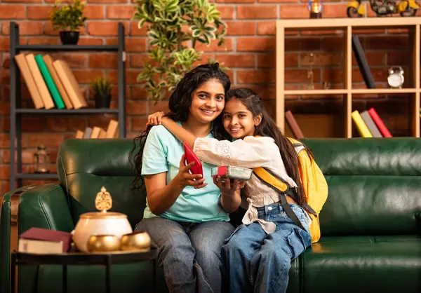 Hintli Asyalı genç anne okuldan önce sevgi dolu bir şekilde küçük kızına beslenme çantasını açar ve birlikte şık, modern bir evde otururken heyecanla gülümsemesini sağlar.