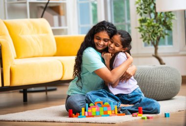 Hint Asyalı genç anne ve küçük kızı renkli ahşap oyuncaklar kullanarak ev inşa ederken modern müsrif bir evin halılı zemininde birlikte oturuyorlar ve kapalı alanda kaliteli zaman geçiriyorlar.