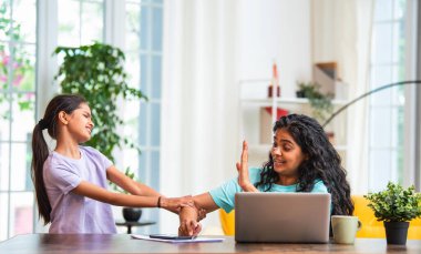 Hintli Asyalı genç anne, modern evdeki dizüstü bilgisayarında çalışırken, sevimli küçük kızı dikkat çekmek için elini çekerek, iş-yaşam dengesi mücadelesi sergiliyor.