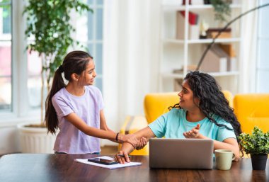 Hintli Asyalı genç anne, modern evdeki dizüstü bilgisayarında çalışırken, sevimli küçük kızı dikkat çekmek için elini çekerek, iş-yaşam dengesi mücadelesi sergiliyor.