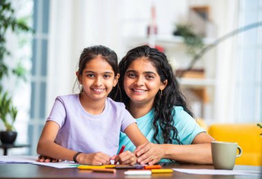 Hintli Asyalı küçük kız, modern bir evde masasında otururken pastel boya kalemleriyle resim çizmeye odaklanmış. Genç annesi de onun yaratıcılığını, sanatını ve adanmışlığını takdir ediyor.