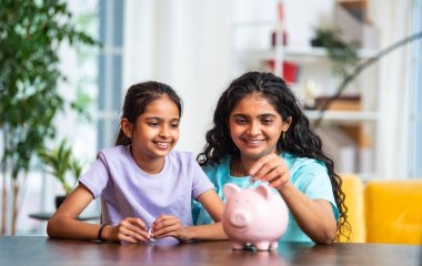 Hintli Asyalı genç bir kadın ve şirin küçük bir kız birlikte para biriktiriyorlar, modern evdeki masa başındaki pembe domuzcuk bankasına para koyuyorlar, erken tasarruf alışkanlıklarını, disiplini, finansal okur yazarlığı öğretiyorlar.