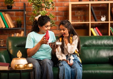 Hintli Asyalı genç anne okuldan önce sevgi dolu bir şekilde küçük kızına beslenme çantasını açar ve birlikte şık, modern bir evde otururken heyecanla gülümsemesini sağlar.