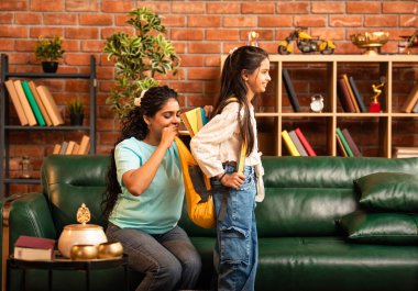 Hintli bir anne, kızının okula gitmesine yardım etmek için kitap paketliyor, okul çantasına beslenme çantası koyuyor, ona sevgiyle sarılıyor ve sıcak bir ev ortamında şefkatle onu uğurluyor.