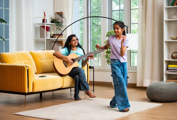 Hint Asyalı genç bir anne akustik gitar çalarken küçük kızı geniş ve modern bir evde neşeyle dans ediyor. Sevgisini gösteriyor, aile bağı kuruyor, eğleniyor ve birlikte zaman geçiriyor.