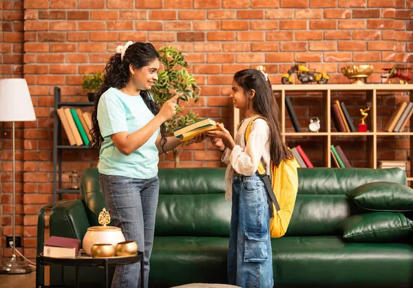 Hintli bir anne, kızının okula gitmesine yardım etmek için kitap paketliyor, okul çantasına beslenme çantası koyuyor, ona sevgiyle sarılıyor ve sıcak bir ev ortamında şefkatle onu uğurluyor.