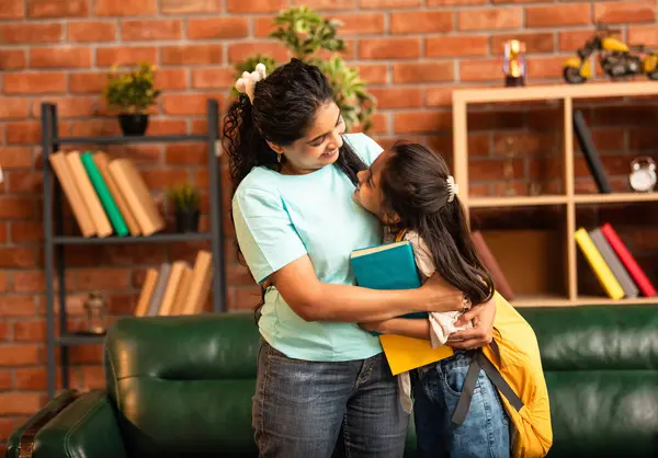 Hintli bir anne, kızının okula gitmesine yardım etmek için kitap paketliyor, okul çantasına beslenme çantası koyuyor, ona sevgiyle sarılıyor ve sıcak bir ev ortamında şefkatle onu uğurluyor.