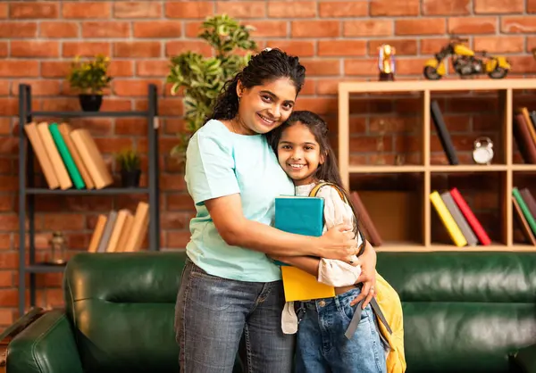 Hintli bir anne, kızının okula gitmesine yardım etmek için kitap paketliyor, okul çantasına beslenme çantası koyuyor, ona sevgiyle sarılıyor ve sıcak bir ev ortamında şefkatle onu uğurluyor.