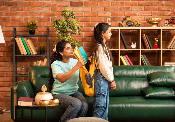 Hintli bir anne, kızının okula gitmesine yardım etmek için kitap paketliyor, okul çantasına beslenme çantası koyuyor, ona sevgiyle sarılıyor ve sıcak bir ev ortamında şefkatle onu uğurluyor.