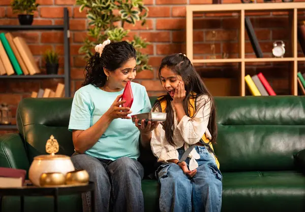 Hintli Asyalı genç anne okuldan önce sevgi dolu bir şekilde küçük kızına beslenme çantasını açar ve birlikte şık, modern bir evde otururken heyecanla gülümsemesini sağlar.