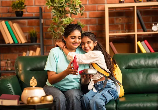 Hintli Asyalı genç anne okuldan önce sevgi dolu bir şekilde küçük kızına beslenme çantasını açar ve birlikte şık, modern bir evde otururken heyecanla gülümsemesini sağlar.