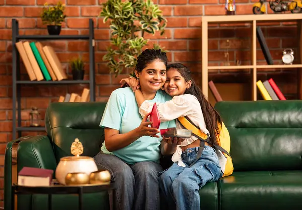 Hintli Asyalı genç anne okuldan önce sevgi dolu bir şekilde küçük kızına beslenme çantasını açar ve birlikte şık, modern bir evde otururken heyecanla gülümsemesini sağlar.