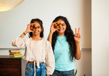 Hintli Asyalı genç bir anne ve şirin küçük bir kız kanepede oturuyor modern bir evde, neşeyle yuvarlak bir çörek tutuyor, delikten bakıyor, gülümsüyor ve iyi bir el hareketi yapıyor.