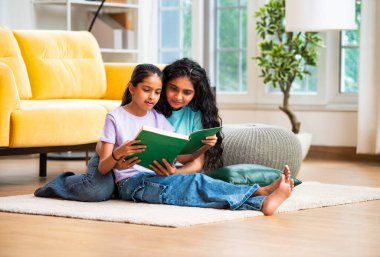 Hintli Asyalı genç anne ve şirin küçük kız şık, modern bir oturma odasında birlikte oturmuş, ilgi ve neşe dolu bir kitap okuyor, eğitici bir bağ kurma zamanının keyfini çıkarıyor, aşkı besliyor.