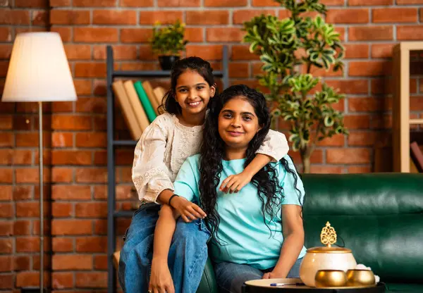 Hintli şirin küçük kız ve genç anne, rahat bir kanepede sırtüstü oturuyor, şakacı bir şekilde birbirlerini sevgiyle itiyorlar, eğlenceli, neşeli ve sevgi dolu bir anı paylaşıyorlar.