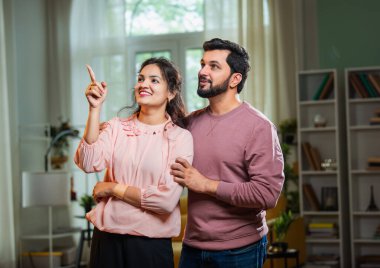 Hintli Asyalı çekici genç çift oturma odasında birlikte durup gülümserken ve heyecanlı görünürken aynı zamanda mutlu ifadelerle umut, fırsat ve yeni bir başlangıcı temsil ediyorlar.