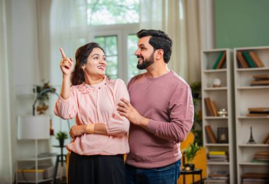 Hintli Asyalı çekici genç çift oturma odasında birlikte durup gülümserken ve heyecanlı görünürken aynı zamanda mutlu ifadelerle umut, fırsat ve yeni bir başlangıcı temsil ediyorlar.