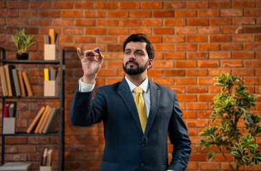 Görünmez cam ekranda yazan, mutlu Hintli genç iş adamı, CEO ya da iş adamı resmi kurumsal kıyafetli, sakallı girişimci terasotta tuğlalı duvarlı sıcak ofise güvenli bir şekilde bakıyor.