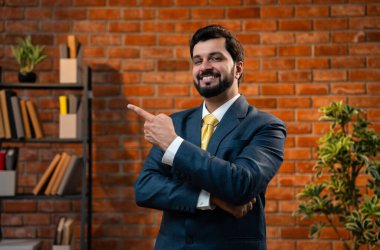 Mutlu Hintli Asyalı genç işadamı ya da CEO 'su sakallı, güvenilir bir şekilde gülümseyen ve yan tarafları işaret eden rahat bir ofiste dururken bir şeyleri destekleyen, reklamını yapan ya da onaylayan.