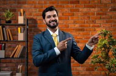 Mutlu Hintli Asyalı genç işadamı ya da CEO 'su sakallı, güvenilir bir şekilde gülümseyen ve yan tarafları işaret eden rahat bir ofiste dururken bir şeyleri destekleyen, reklamını yapan ya da onaylayan.