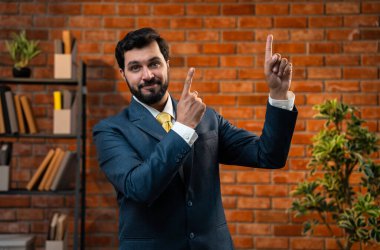 Mutlu Hintli Asyalı genç işadamı ya da CEO 'su sakallı, güvenilir bir şekilde gülümseyen ve yan tarafları işaret eden rahat bir ofiste dururken bir şeyleri destekleyen, reklamını yapan ya da onaylayan.