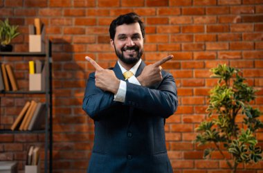 Mutlu Hintli Asyalı genç işadamı ya da CEO 'su sakallı, güvenilir bir şekilde gülümseyen ve yan tarafları işaret eden rahat bir ofiste dururken bir şeyleri destekleyen, reklamını yapan ya da onaylayan.