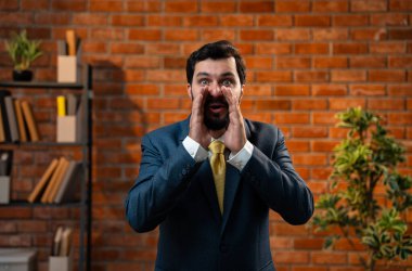 İki eli ağızında bağırarak, Hintli genç iş adamı ya da CEO 'su heyecanlı, sakallı, güzel haberler veren, tuğla duvara karşı samimi bir ofiste duran,