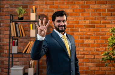 Sayıları gösterirken kendine güvenen parmakları kullanan, resmi kurumsal giyinmiş Hintli Asyalı sakallı ceo işadamı parmaklarını sayarken tuğla duvara karşı samimi bir ofiste duruyor.