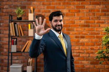 Sayıları gösterirken kendine güvenen parmakları kullanan, resmi kurumsal giyinmiş Hintli Asyalı sakallı ceo işadamı parmaklarını sayarken tuğla duvara karşı samimi bir ofiste duruyor.