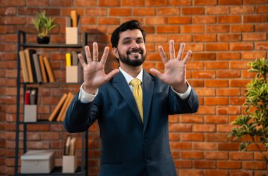 Sayıları gösterirken kendine güvenen parmakları kullanan, resmi kurumsal giyinmiş Hintli Asyalı sakallı ceo işadamı parmaklarını sayarken tuğla duvara karşı samimi bir ofiste duruyor.