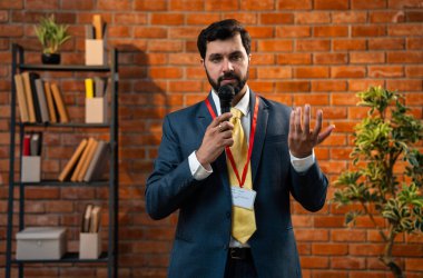 Hintli işadamı mikrofona konuşurken samimi modern ofiste resmi bir konuşma yapıyor. Asya CEO 'su ya da takım elbiseli ve sakallı girişimci kırmızı tuğla duvara yaslanmış duruyor.