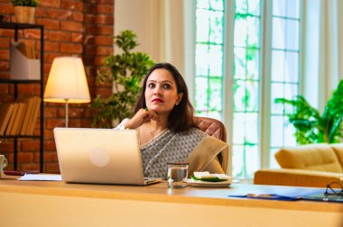 Video konferans konuşmasında kulaklıklı dizüstü bilgisayarla konuşan Hintli genç iş kadını ya da sari içindeki kadın şirket çalışanı uzaktan kumandalı online toplantı sırasında rahat modern ofis masasında oturuyor.