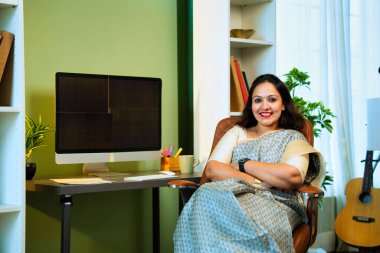 Pazar saatlerinde bilgisayarda çalışan Hintli genç ve başarılı kadın hisse senedi tüccarı ya da sari yatırımcısı rahat ev ofisinden güvenli bir şekilde hisse senedi yatırımlarını yönetirken aynı zamanda gülümseyerek kameraya bakıyor.