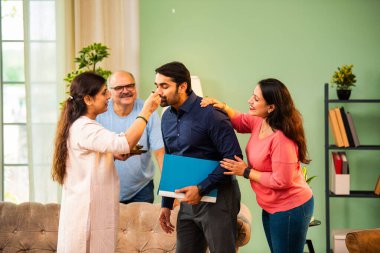 Genç Hintli bir adam iş görüşmesini kırar, üst düzey ebeveynler ve kız kardeşlerle tanışmak için yönetici kıyafetiyle eve döner, aileye sarılır, kutsanmak ister, başarıyı kutlar ve neşeli duygusal anı paylaşır.