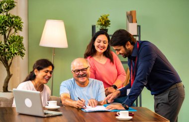 Hintli kıdemli bir adam, genç yönetici olarak belgeyi imzalarken ona yol gösteriyor. Rahat modern bir evde eşi ve kızının yanında oturuyor. Vasiyeti, yasal belgeleri, finans veya sigorta danışmanlığını sembolize ediyor.