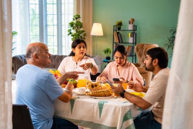 Birlikte kahvaltı ederken, Hintli üst düzey ebeveynler ve genç yetişkin kız ve erkek çocuk yemek masasında rahat, modern bir evde oturmuş yemek saatinde akıllı telefon kullanımı ve dijital dikkat dağınıklığı üzerine tartışıyorlardı.