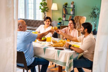 Neşeli tostlar içinde samosa yetiştirmek, mutlu Hintli aile üst düzey ebeveynler ve genç yetişkin kız ve erkek çocuklar sabahları modern sıcak ev yemeği masasında keyifli bir kahvaltı yapıyorlar.