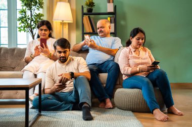 Akıllı telefonlar kullanarak kanepede oturmak, Hintli ailelerin aileleri modern rahat oturma odalarında küçük çocuklar, hepsi mobil ekran bağımlısı bir aile olarak etkileşim ya da bağ kurma zamanı olmadan