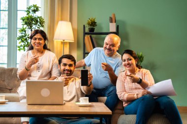 Boş bir telefon ekranı, dört çocuklu Hintli aile, evde rahat bir koltukta oturmuş gülümseyen ve kameraya uygulamayı veya servisi destekleyen yetişkin aile ve çocuklar.